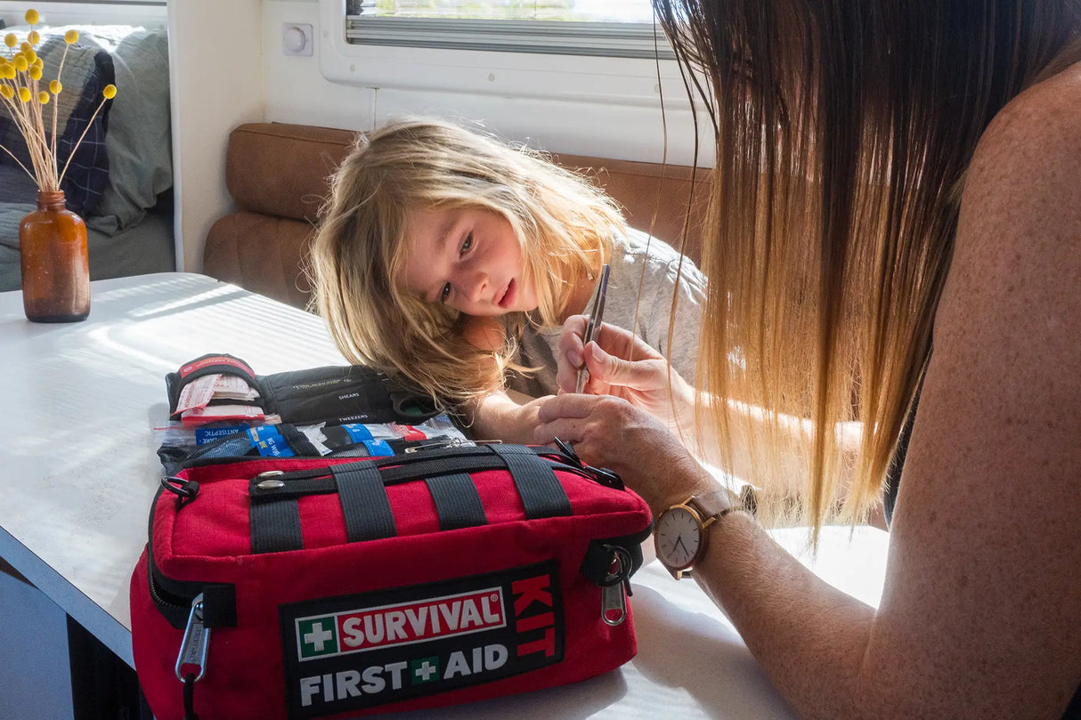 A mother using the tweezers from the SURVIVAL Family First Aid KIT to remove a foreign object from under her son's fingernail.